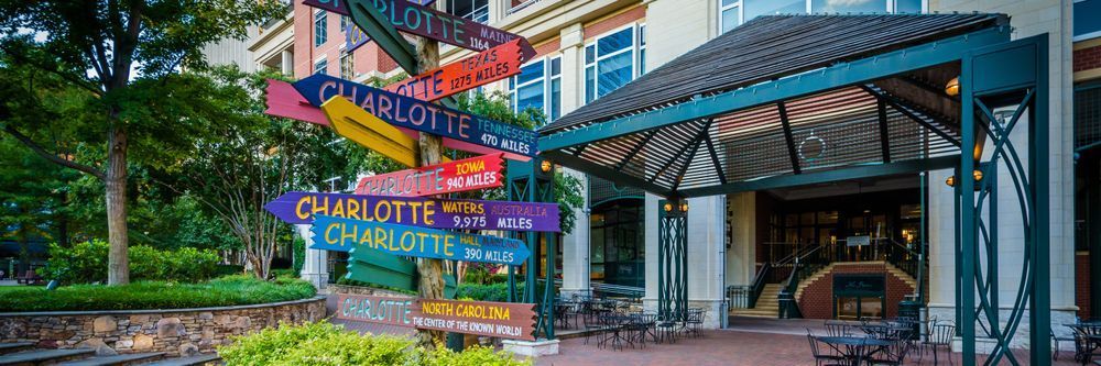 Colorful directional signposts indicating distances to various cities from charlotte, north carolina, set in a quaint urban park with seating and greenery.