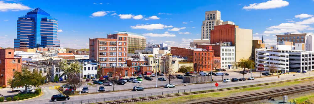 Panoramic view of a modern urban skyline with a mix of high-rise buildings and historic architecture, featuring a rail road in the foreground under a clear blue sky.