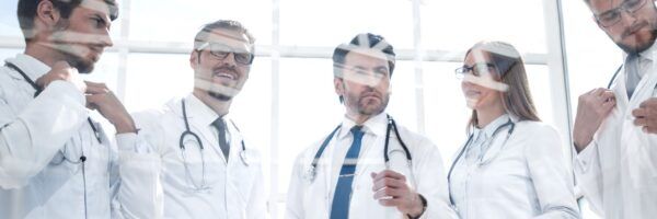 A group of five medical professionals in Dallas, wearing white lab coats and stethoscopes, engaged in a discussion in a bright, modern office with large windows.