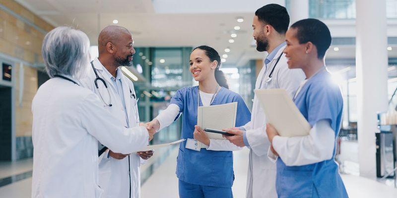 Three female nurses in scrubs, smiling and conversing while holding clipboards and notebooks in a hospital corridor, are majoring in Allied Health.